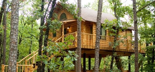 A wooden treehouse nestled among trees, featuring a balcony and rustic design.