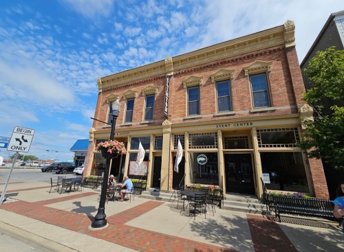 Historic brick building with an event center sign, outdoor seating, and a blue sky with scattered clouds.