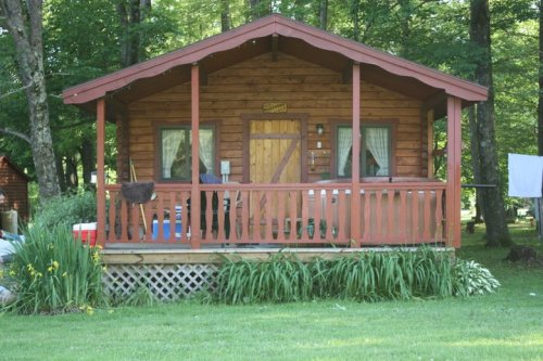 A cozy wooden cabin with a porch, surrounded by greenery and flowers, set in a peaceful outdoor environment.