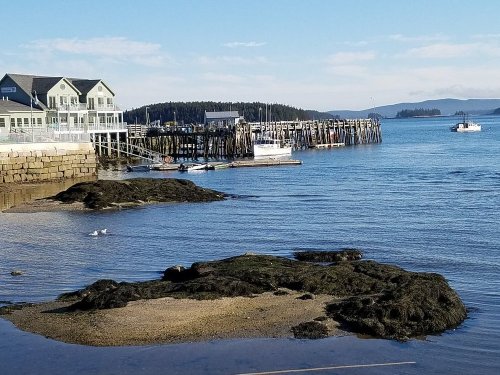 A serene coastal scene featuring a pier, boats, and rocky shoreline under a clear blue sky.