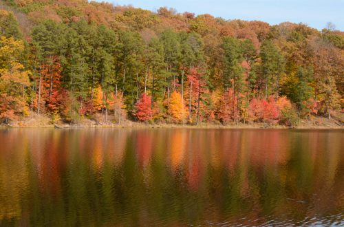 A serene lake reflecting vibrant autumn foliage in shades of red, orange, and yellow, surrounded by trees.