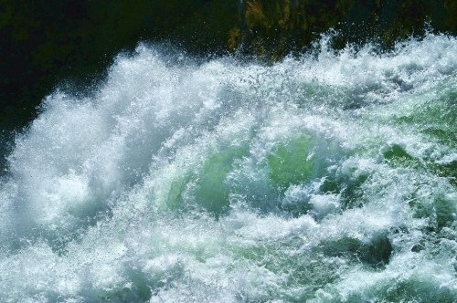 A close-up of turbulent, frothy water with swirling green and white waves.