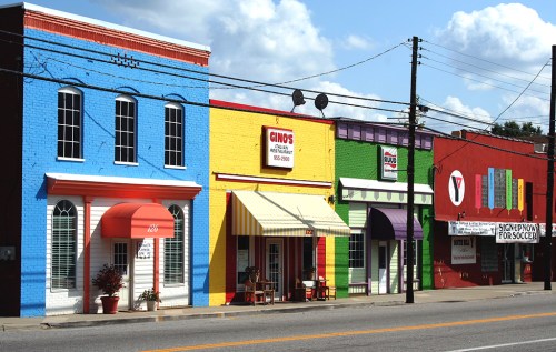 Colorful storefronts line a street, featuring bright blue, yellow, green, and red buildings with awnings and signage.