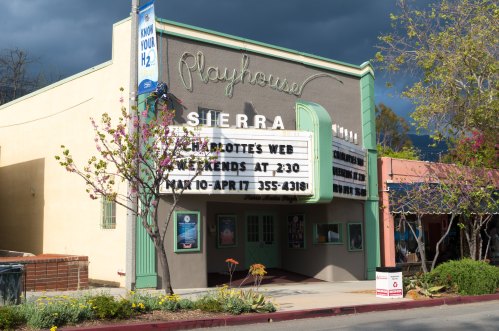 The Sierra Playhouse marquee displays "Charlotte's Web" with showtimes on a cloudy day. Flowers bloom nearby.