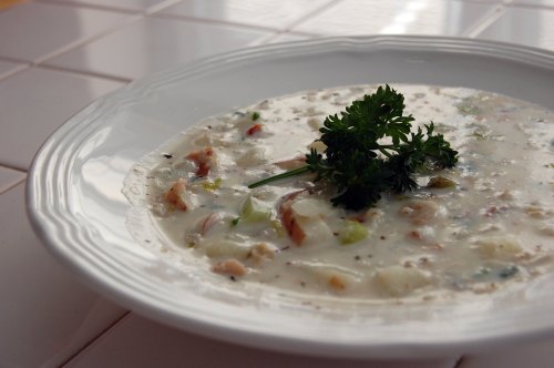 A bowl of creamy soup garnished with parsley, featuring chunks of vegetables and meat on a white plate.
