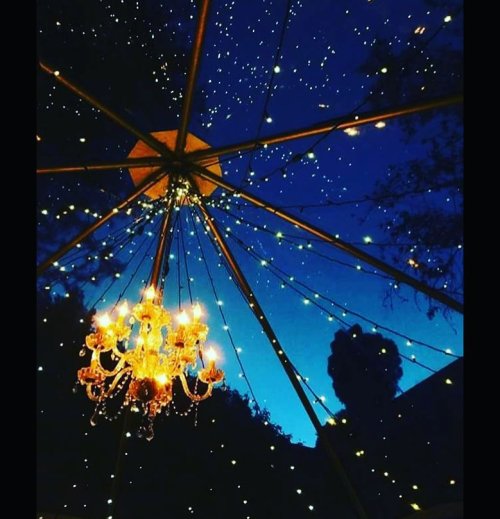 A chandelier hangs beneath a starry sky, with twinkling lights illuminating a tent structure.