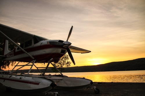 A seaplane on the shore at sunset, with calm water and hills in the background.