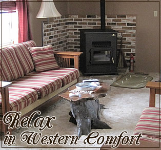 Cozy living room with striped sofas, a rustic coffee table, and a wood stove against a brick wall. Text: "Relax in Western Comfort."