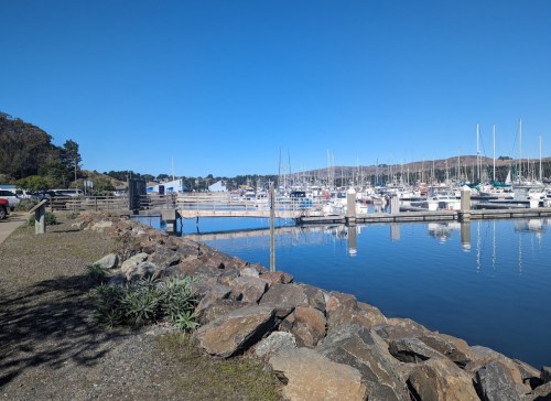 A serene marina with boats docked, surrounded by rocky shores and clear blue skies.