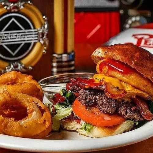 A juicy burger with cheese, bacon, lettuce, and tomato, served with onion rings and dipping sauce on the side.