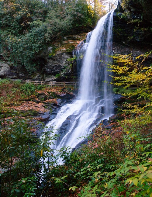 A serene waterfall cascades down rocky cliffs, surrounded by lush greenery and autumn foliage.