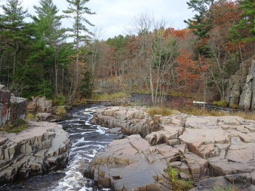 A serene landscape featuring a flowing river surrounded by rocky terrain and autumn-colored trees.