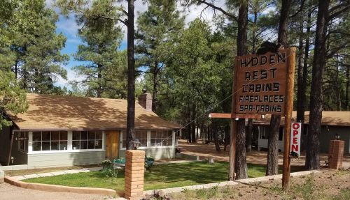 A rustic cabin with a sign reading "Hidden Rest Cabins" surrounded by trees and a grassy area.