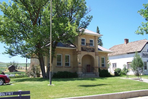 Historic building with a sign, surrounded by trees and grass, under a clear blue sky. Nearby structures visible.