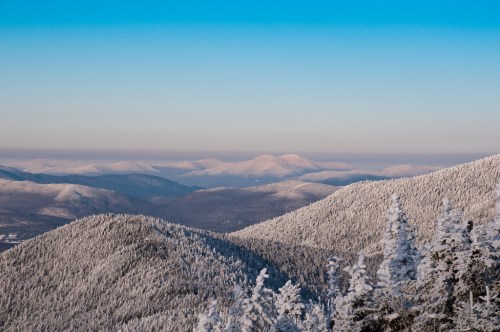 Snow-covered mountains under a clear blue sky, with layers of peaks fading into the distance.