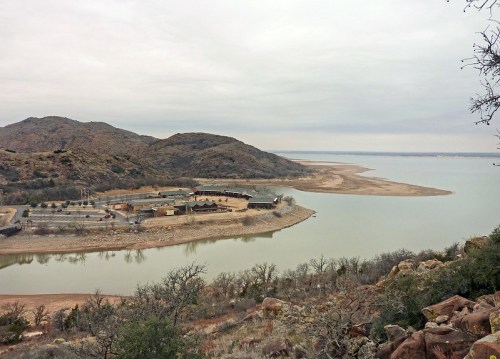 A serene landscape featuring a lake surrounded by hills and sparse vegetation under a cloudy sky.