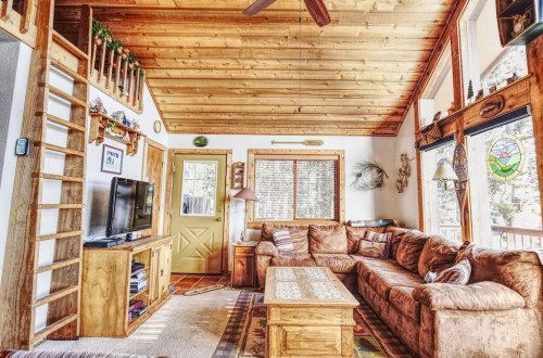 Cozy living room with wooden ceiling, large couch, TV, and a door leading outside, decorated with rustic accents.