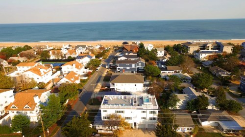 Aerial view of a coastal neighborhood with houses, trees, and a sandy beach along the ocean.