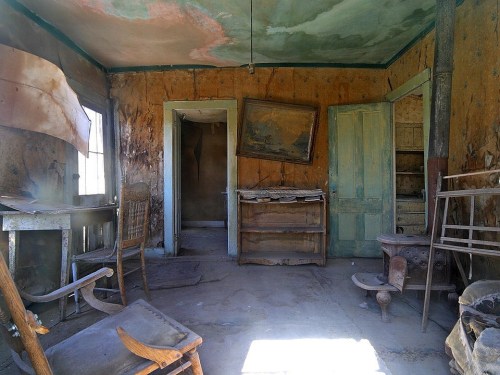 Abandoned room with peeling walls, old furniture, and two doors leading to other spaces. Dusty and neglected atmosphere.
