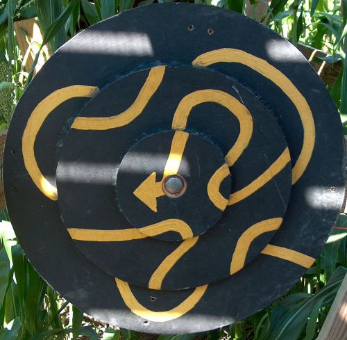 A circular target with a black background and yellow swirling lines, featuring an arrow pointing left at the center.
