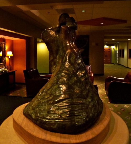 A bronze sculpture of a couple dancing, set in a warmly lit lobby with comfortable seating.