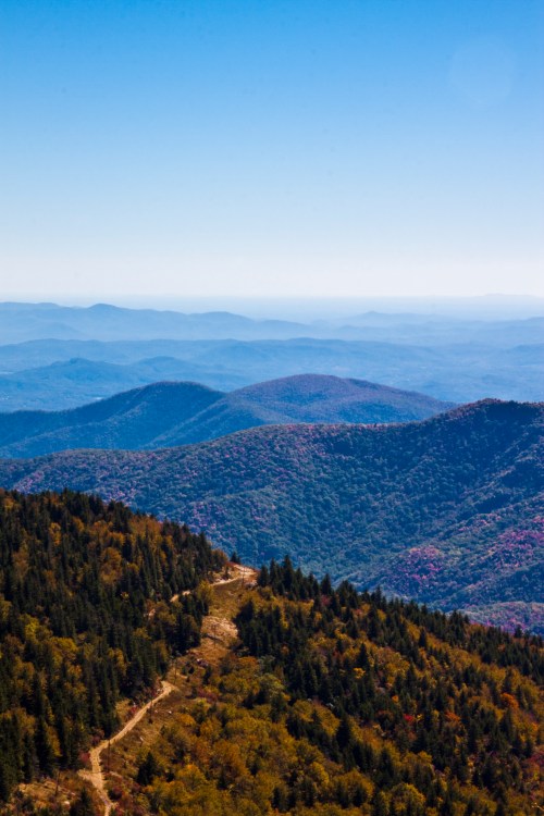 A panoramic view of rolling mountains with lush greenery and a clear blue sky in the background.