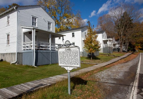 A row of white houses along a grassy area, with a historical marker in the foreground and a clear blue sky above.