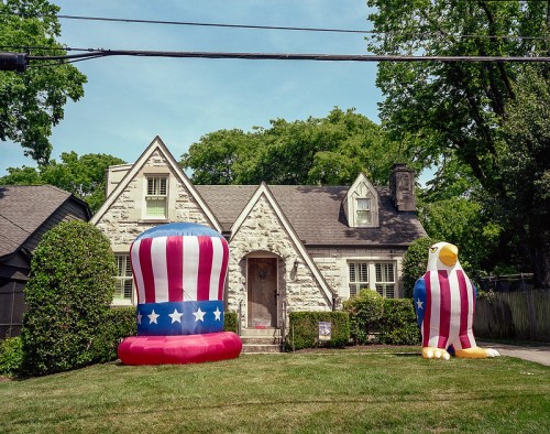 A house with large inflatable patriotic decorations: a tall striped hat and an eagle, set in a green yard.