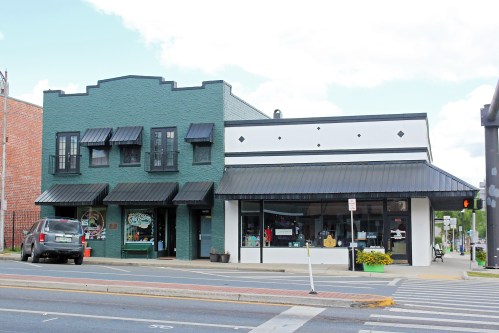 Two storefronts side by side: one green with black awnings, the other white with decorative accents, on a city street.