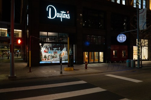 Nighttime view of Dayton's storefront with festive window display and city street in front.
