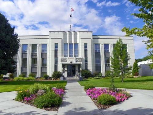 Art Deco-style building with large windows, surrounded by green grass and colorful flower beds under a blue sky.