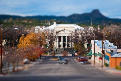 A blurred view of a town square with a historic building, autumn trees, and distant mountains in the background.