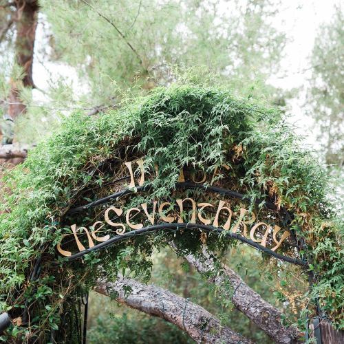 A decorative arch covered in greenery with the words "In the Seventh Kay" displayed prominently.