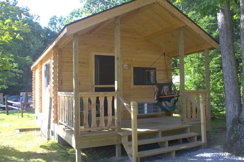 A wooden cabin with a porch and a swing, surrounded by trees in a natural setting.