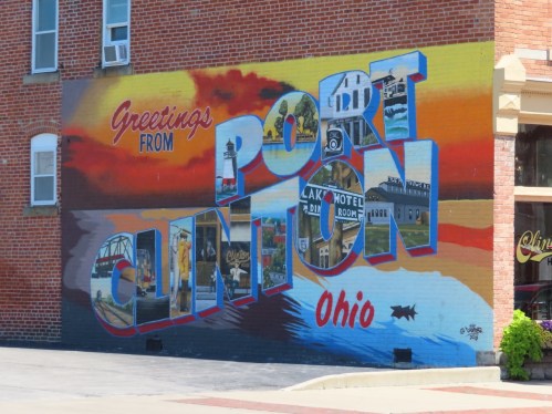 Colorful mural reading "Greetings from Port Clinton, Ohio" with scenic images and a sunset background.