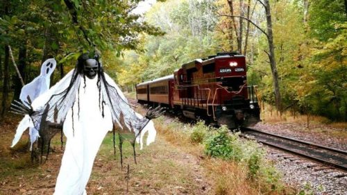 A ghostly figure stands beside a train on a tree-lined track, surrounded by autumn foliage.
