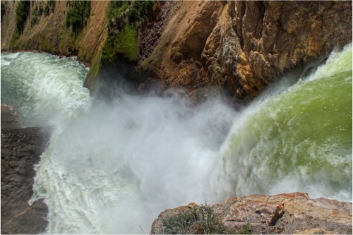 A powerful waterfall cascades over rocky cliffs, creating mist and vibrant green water in a natural landscape.