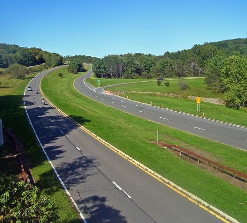 A winding highway surrounded by green trees and grass under a clear blue sky.