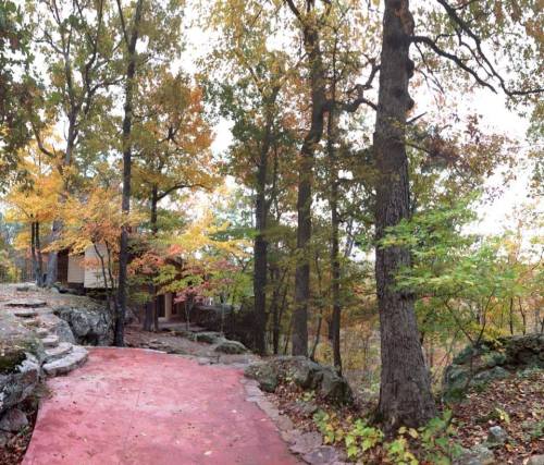 A winding path leads through colorful autumn trees to a cozy cabin nestled among the rocks.
