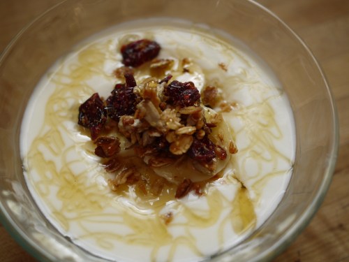 A bowl of yogurt topped with granola, dried fruit, and a drizzle of honey.