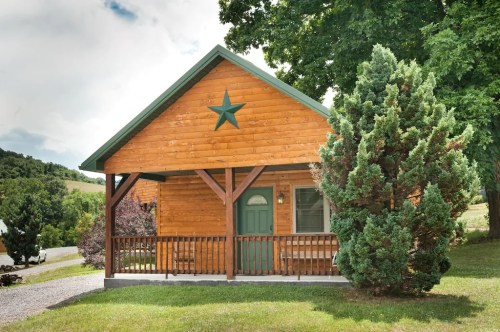 A wooden cabin with a green door and star decoration, surrounded by trees and a gravel path.