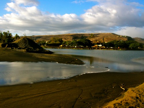 A serene landscape featuring a calm river, sandy shore, and distant hills under a partly cloudy sky.