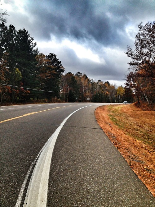 A winding road surrounded by trees and autumn foliage under a cloudy sky.