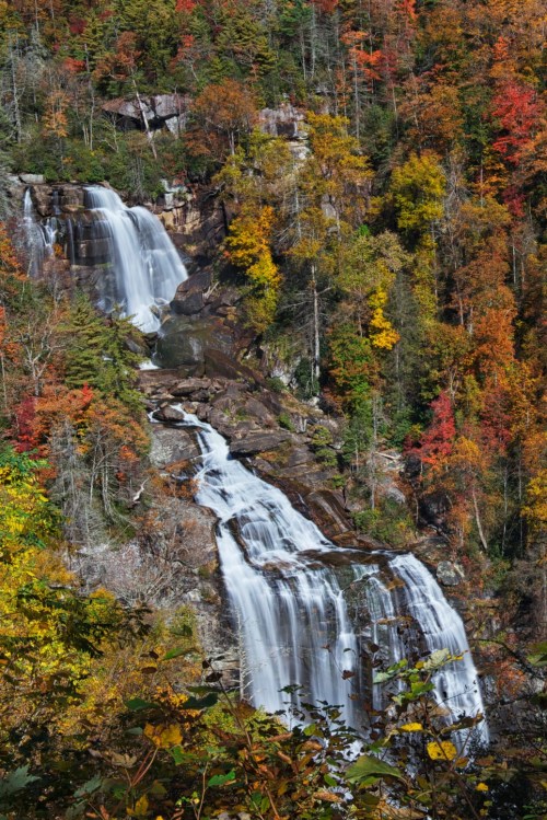 A scenic waterfall cascading down rocky cliffs, surrounded by vibrant autumn foliage in shades of orange and yellow.