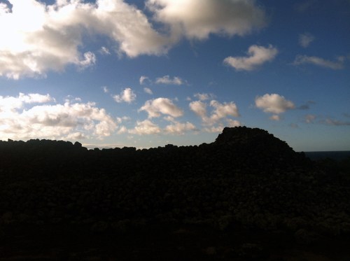 Silhouette of a stone structure against a cloudy sky, with ocean visible in the background.
