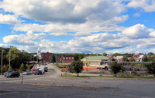A scenic view of a town with a road, buildings, and a cloudy blue sky in the background.