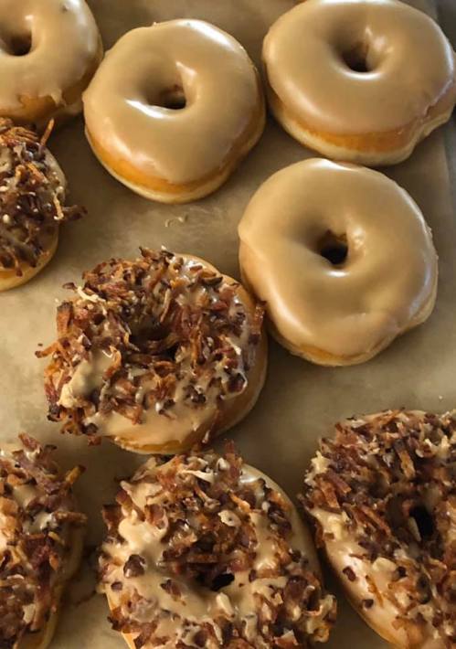 A variety of donuts: some glazed and others topped with coconut and nuts, arranged on parchment paper.