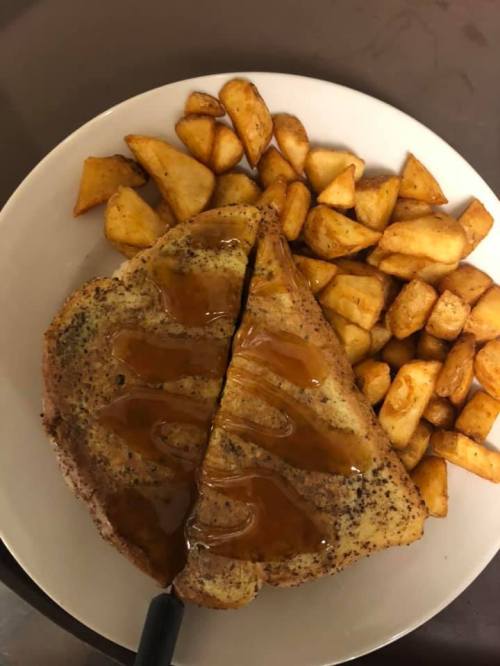 A plate of French toast drizzled with syrup, accompanied by golden-brown potato wedges.
