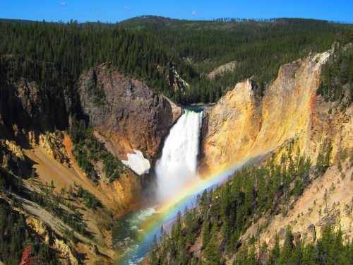 A stunning waterfall cascades into a canyon, surrounded by lush green trees and a vibrant rainbow in the mist.