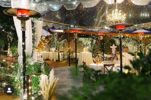 A beautifully decorated outdoor venue with string lights, chandeliers, and tables set for an elegant event.